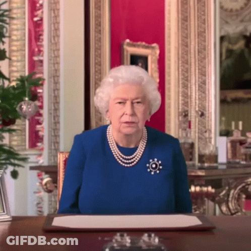 Queen Elizabeth Wearing A Blue Dress And Pearls Sits At A Table GIF