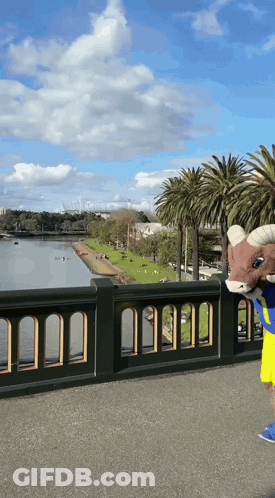 Ram Mascot Standing On Bridge Overlooking River GIF