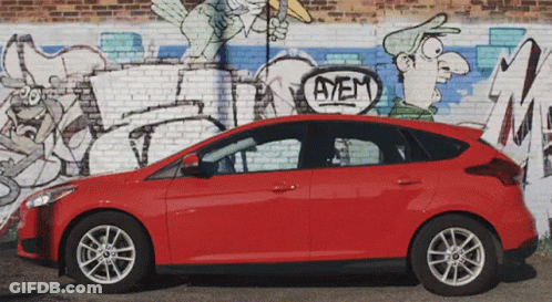 Red Car Parked In Front Of Brick Wall With Graffiti Saying Ayem GIF
