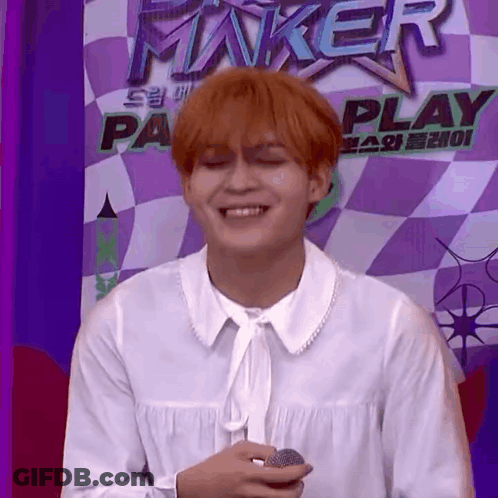Red-Haired Man Holding Microphone In Front Of Checkered Wall GIF