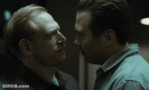 Red-Haired Man With Mustache Talking To Another Man In Dark Room GIF