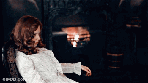 Red-Haired Woman Sitting In Chair By Fire GIF