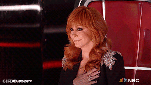 Red-Haired Woman Sitting With Hand On Chest NBC Logo GIF