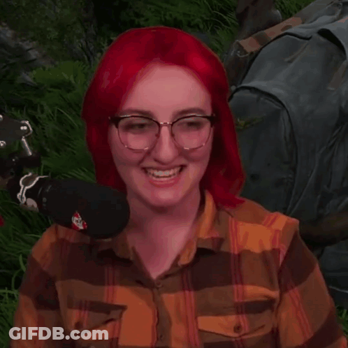 Red-Haired Woman With Glasses Sitting In Grass With Microphone GIF