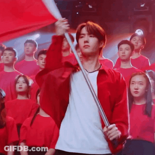 Red Jacket Man Holds Red Flag Before Crowd GIF