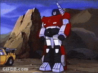 Red Robot With Horn Standing In Front Of Yellow Truck GIF