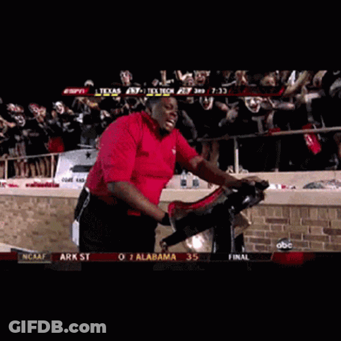 Red Shirt Man Riding Exercise Bike With Masked Crowd GIF