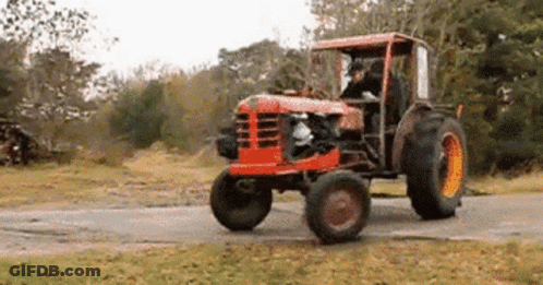 Red Tractor Driving Down Dirt Road In Field GIF