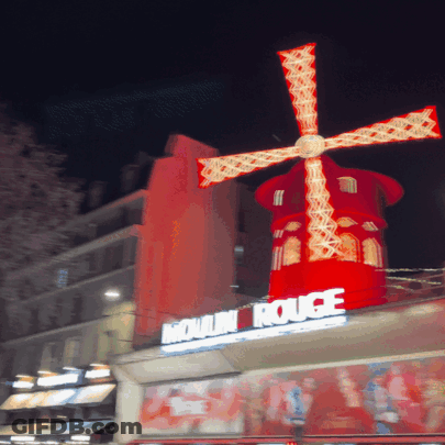 Red Windmill Lit Up In Front Of Moulin Rouge Sign GIF