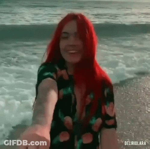 Redhead Woman Holding Man's Hand On Beach GIF