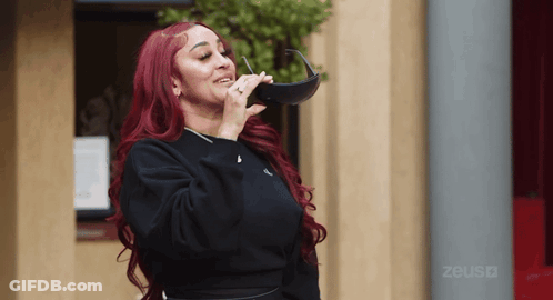 Redhead Woman Holding Sunglasses In Front Of Zeus Building GIF