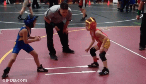 Referee Watching Two Boys Wrestle On Red Mat GIF
