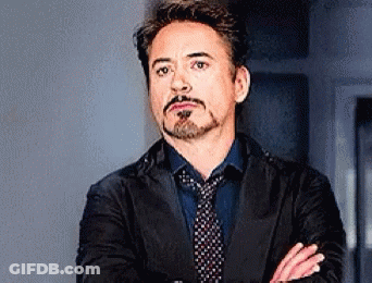 Robert Downey Jr. Is Wearing A Suit And Tie With His Arms Crossed And A Beard . GIF