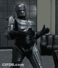 Robot In Suit Giving Thumbs Up In Living Room GIF