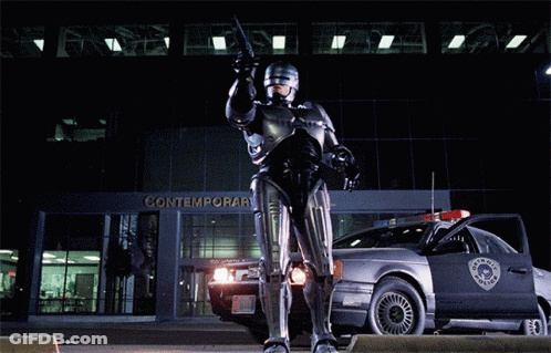 Robot Standing In Front Of Contemporar Building GIF