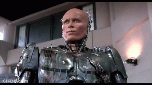 Robot With Bald Head Standing In Room With Wall Light GIF