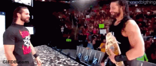 Roman Reigns And Seth Rollins Are Standing Next To Each Other On A Stage . GIF
