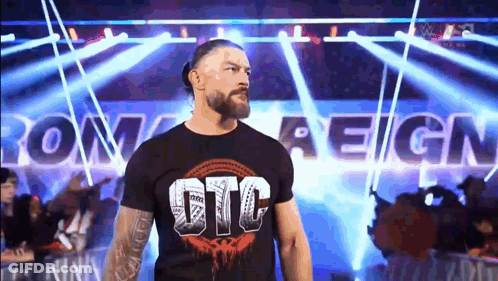 Roman Reigns Is Walking Out Of The Ring Wearing A Black T-Shirt With The Word Reign On It . GIF