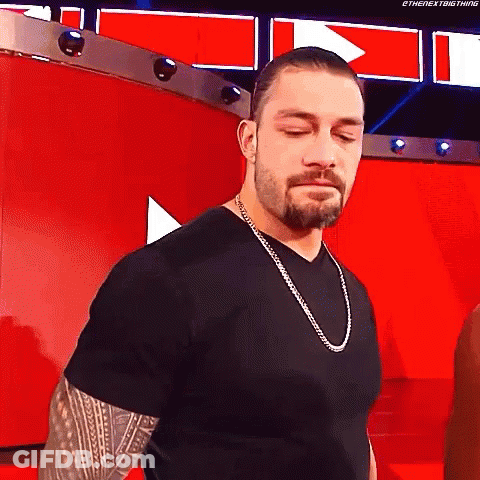 Roman Reigns Is Wearing A Black T-Shirt And A Silver Chain Around His Neck . GIF