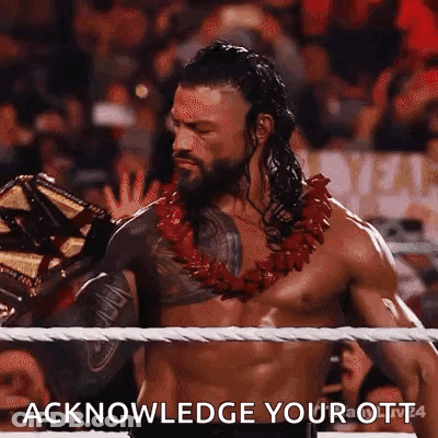 Roman Reigns Is Wearing A Lei And Holding A Wrestling Championship Belt In A Wrestling Ring . GIF