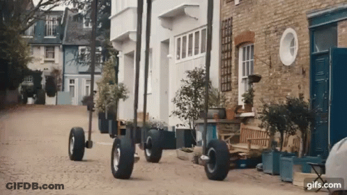 Row Of Houses On Cobblestone Street With Large Wheels GIF