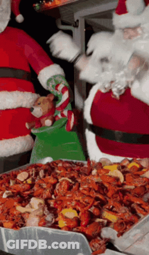 Santa Claus Is Holding A Stuffed Animal While Standing Next To A Tray Of Crawfish GIF