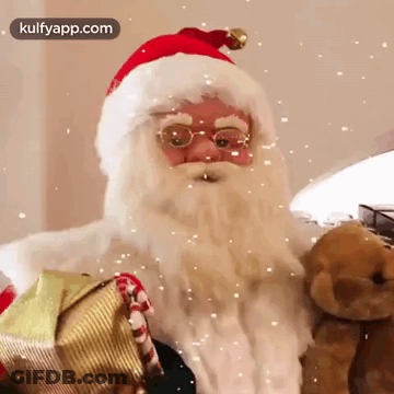 Santa Claus Is Holding A Teddy Bear And A Gift Box While Snow Falls Around Him . GIF