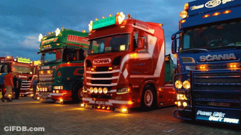 Several Scania Trucks Are Parked In A Row At Night GIF