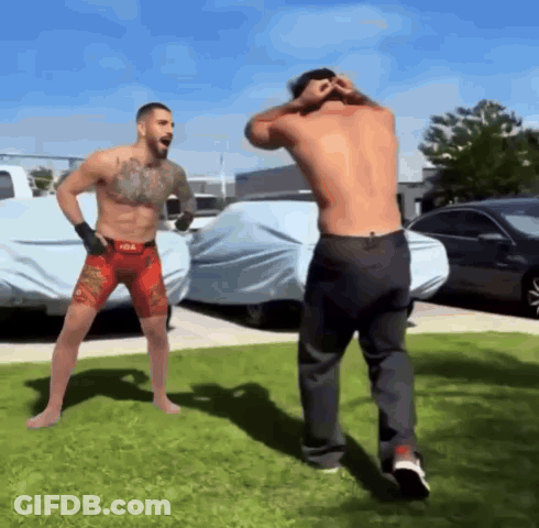 Shirtless Fighter In Red Shorts Next To Shirtless Fighter In Black Jeans GIF