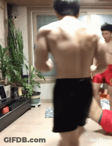 Shirtless Man In Black Shorts Standing With Plants GIF