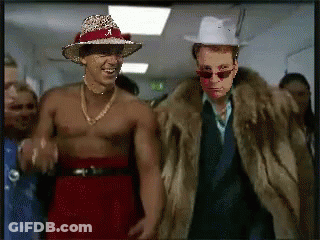 Shirtless Man In Cowboy Hat And Fur Coat Next To Another Man GIF
