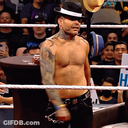Shirtless Man In Fedora In Wrestling Ring With Sign Saying H GIF