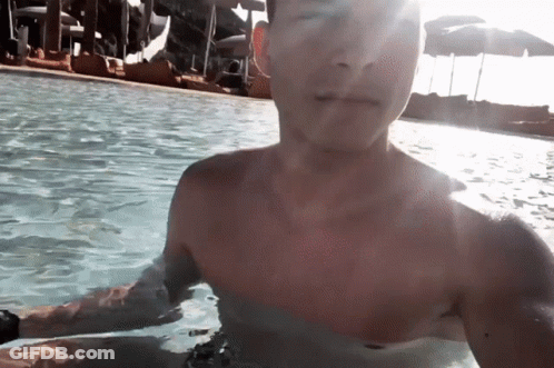 Shirtless Man In Pool With Umbrellas GIF