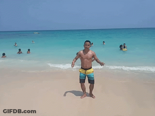 Shirtless Man On Beach Giving Peace Sign GIF