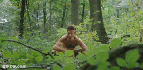 Shirtless Man Sitting In Woods Eating Leaf GIF