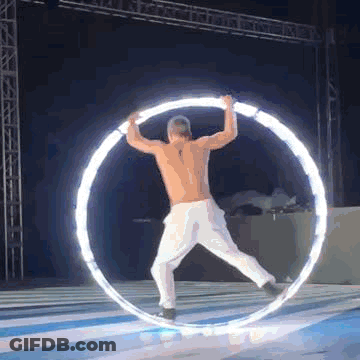 Shirtless Man Spinning Lighted Hula Hoop On Stage GIF