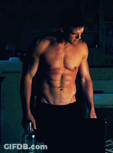 Shirtless Man Standing Hands On Hips In Dark Room GIF