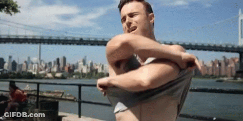 Shirtless Man Taking Off Shirt In Front Of Bridge GIF