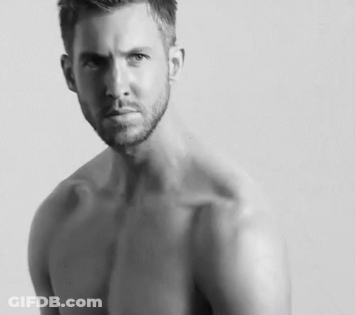 Shirtless Man With Arm Tattoo Sitting Cross-Legged GIF