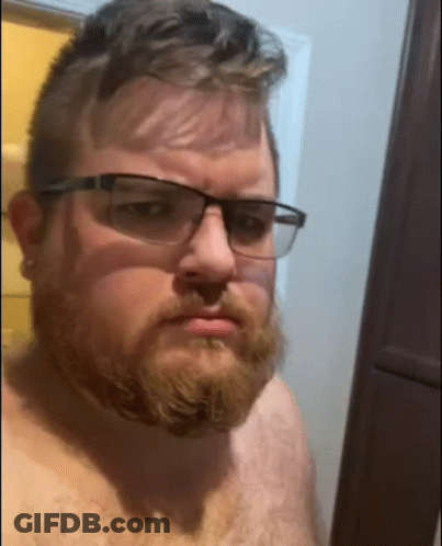 Shirtless Man With Beard And Glasses Taking Selfie In Bathroom GIF