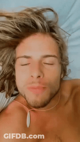 Shirtless Man With Long Blonde Hair Laying On Bed Eyes Closed Necklace GIF