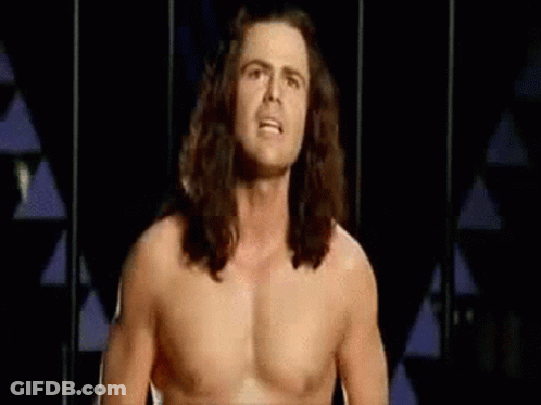 Shirtless Man With Long Hair Standing In Front Of Triangle Wall GIF