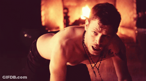 Shirtless Man With Necklace Crawling In Front Of Fire GIF