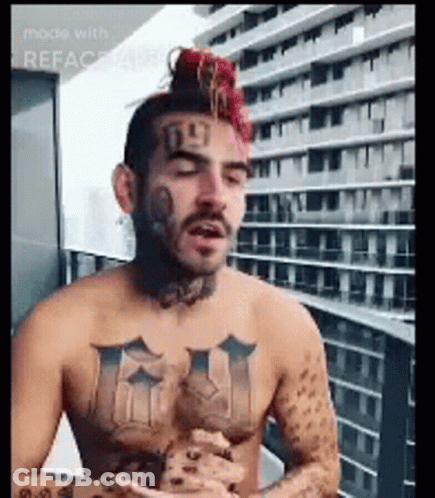 Shirtless Tattooed Man Sitting On Balcony GIF