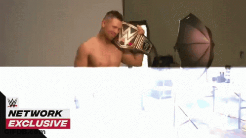 Shirtless Wrestler Holding Wrestling Belt In Front Of Network Exclusive Banner GIF