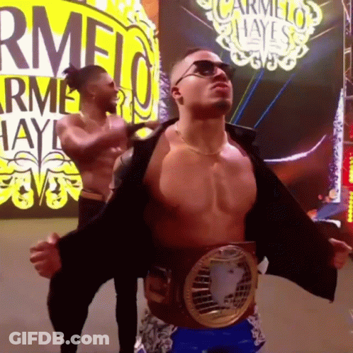 Shirtless Wrestler With Belt In Front Of Carmelo Hayes Sign GIF