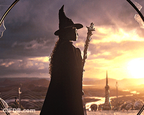 Silhouette Of Woman In Witch Hat Holding Wand In Front Of Sunset GIF