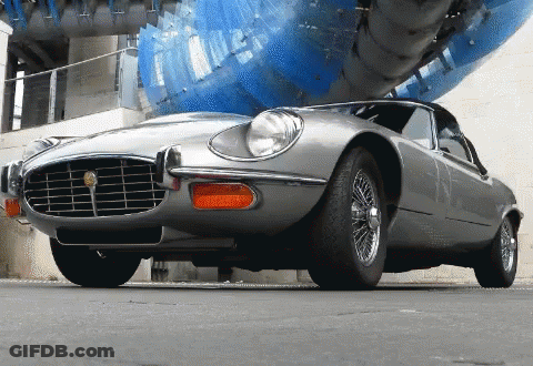 Silver Sports Car Parked In Front Of Blue Sculpture GIF