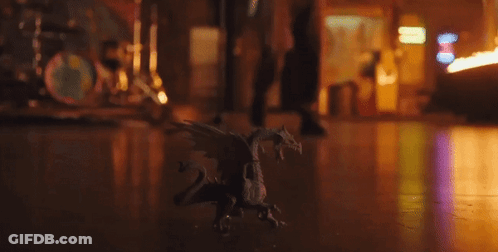 Small Toy Dragon Sitting On Wooden Floor In Dark Room GIF