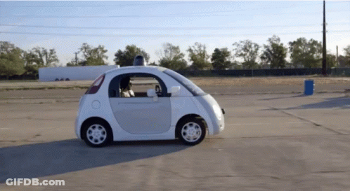 Small White Car Driving Next To Blue Barrel GIF